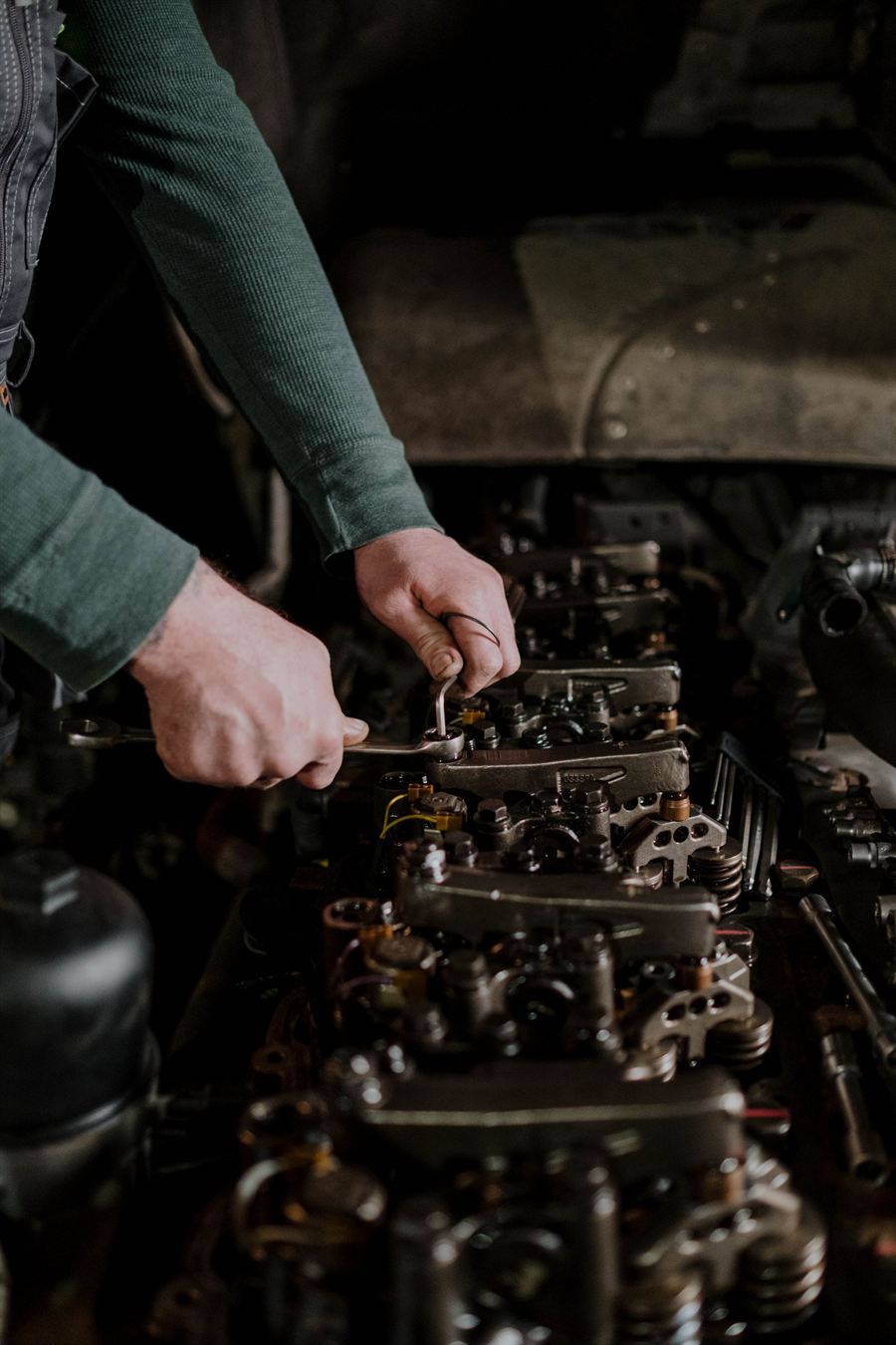 Two hands working a small spanner along the valve gear of a stripped engine.