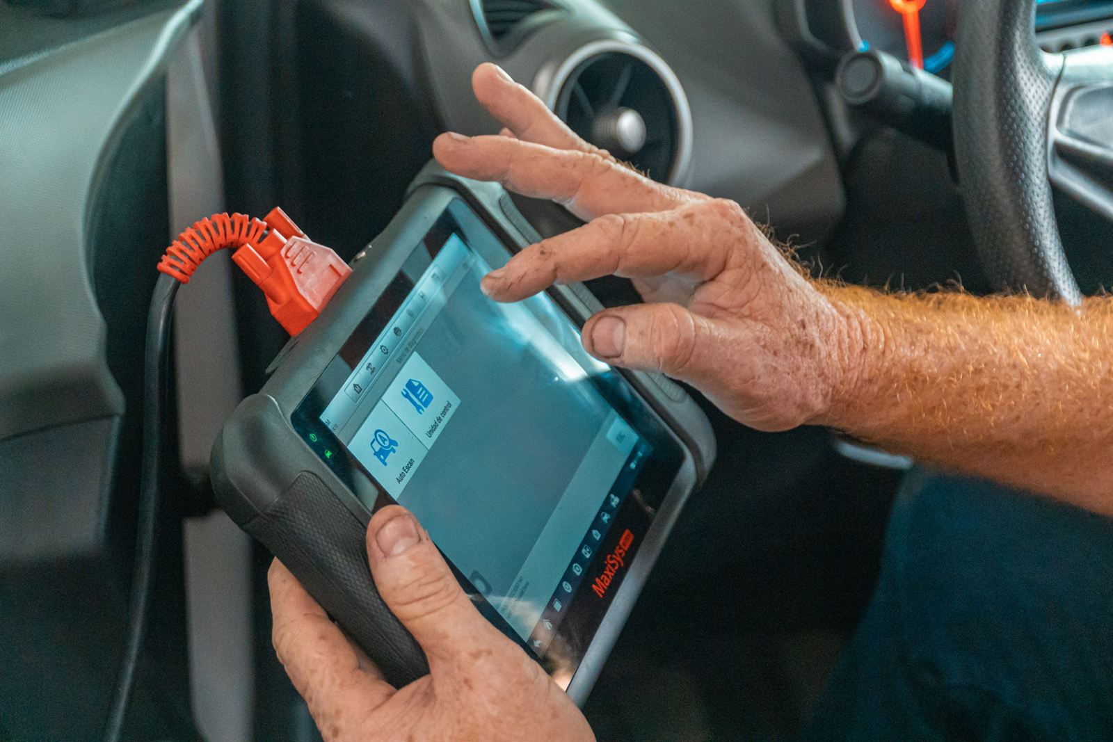 Two hands holding a handheld diagnostic scan tool inside a car, its lead running off to one side.